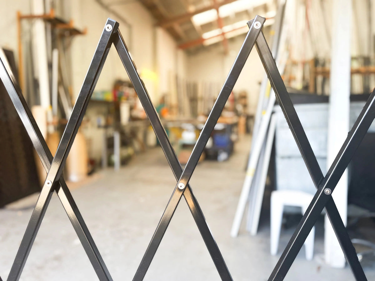 Black expandable barrier with adjustable scissor gate design for pedestrian access control and safety management
